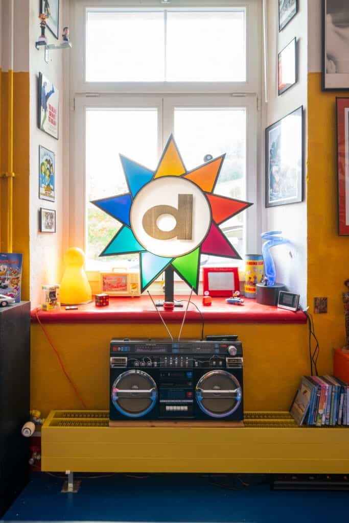 Bunte Garage mit Boombox, Spielzeug und moderner Kunst vor hellen Fenstern.